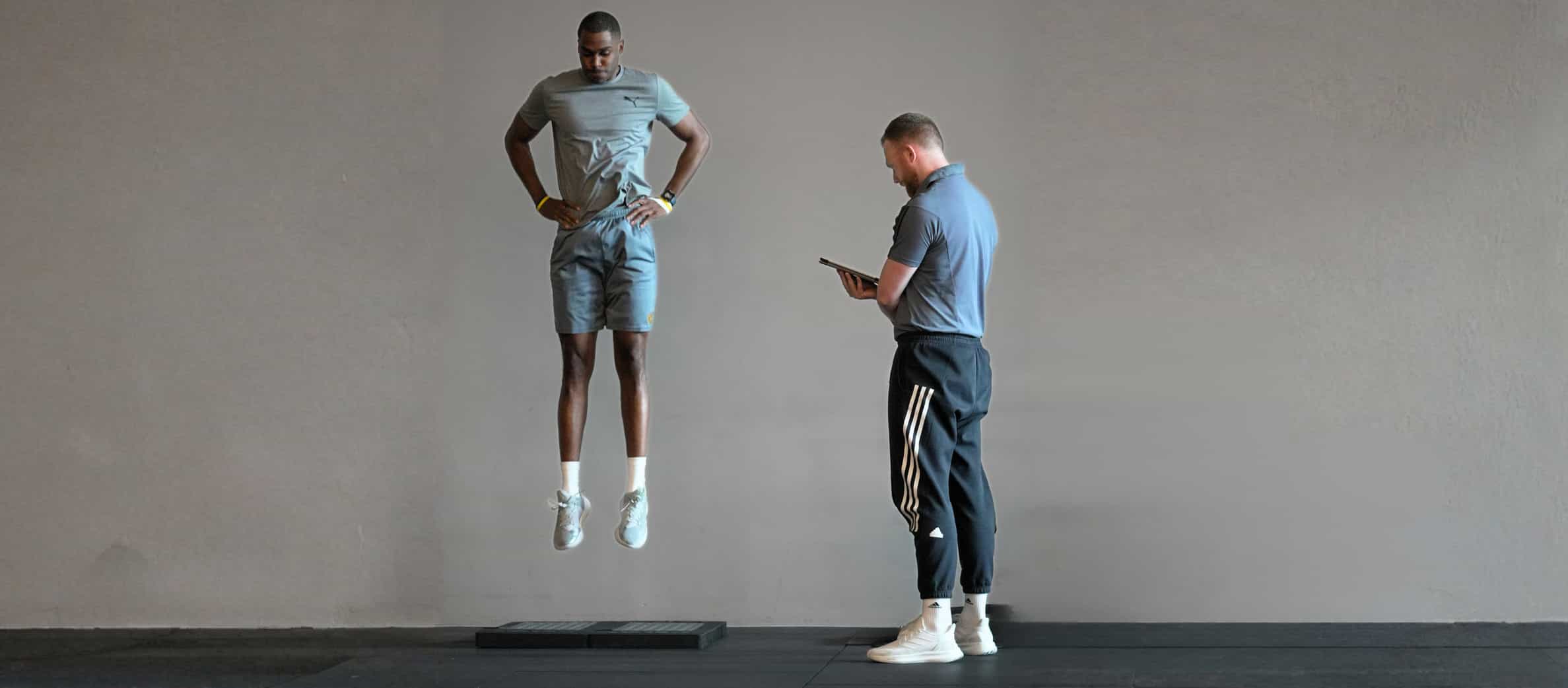 Plyometrisches Training in der späten Reha: Ein Athlet führt einen Sprung über einen Vault aus, während ein Coach Technik und Landung überwacht.