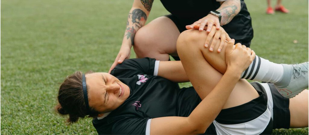 Fußballerin liegt am Boden und hält sich mit schmerzverzerrtem Gesicht das Knie nach einer Kreuzbandverletzung während eines Spiels.