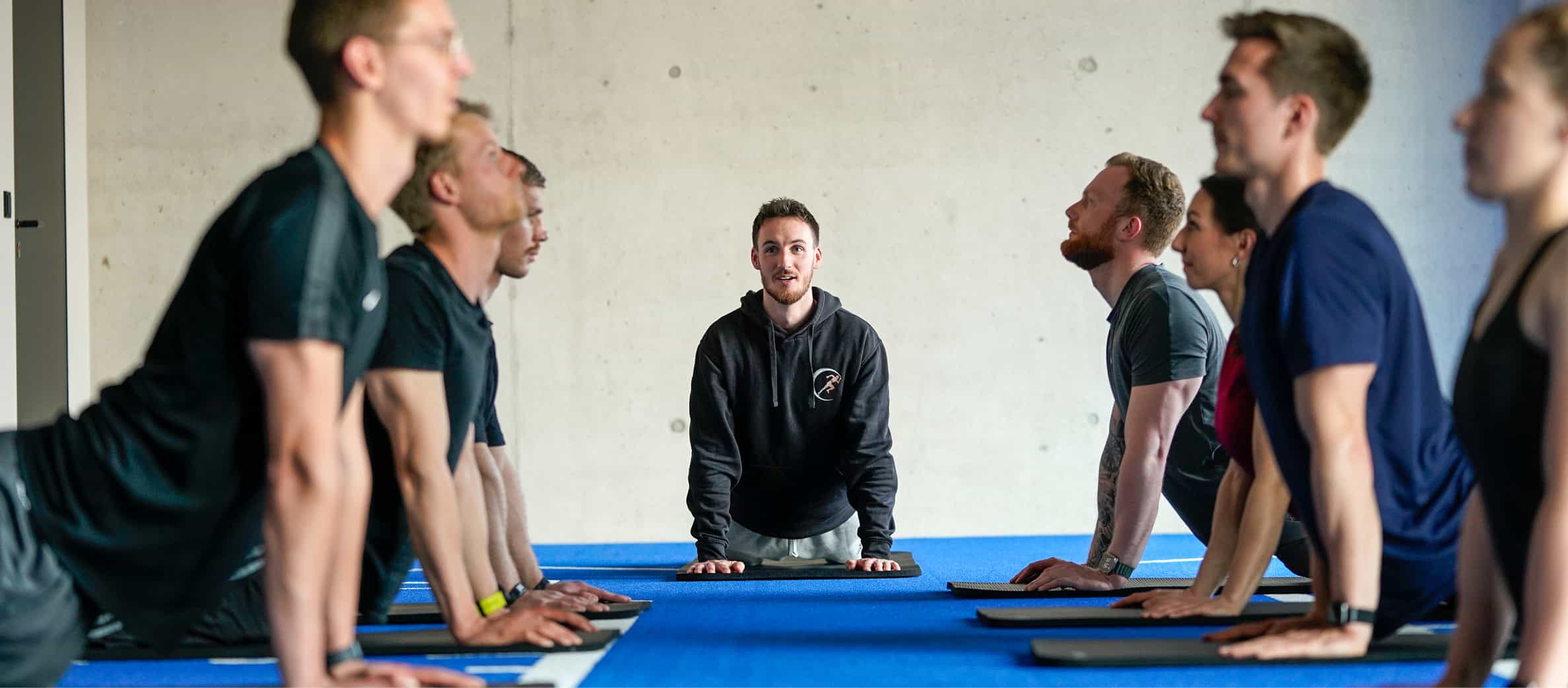 Eine Gruppe von Sportlern führt unter Anleitung eines Trainers eine Yoga-Übung im Foundation Training aus, um die Beweglichkeit der Wirbelsäule zu verbessern.