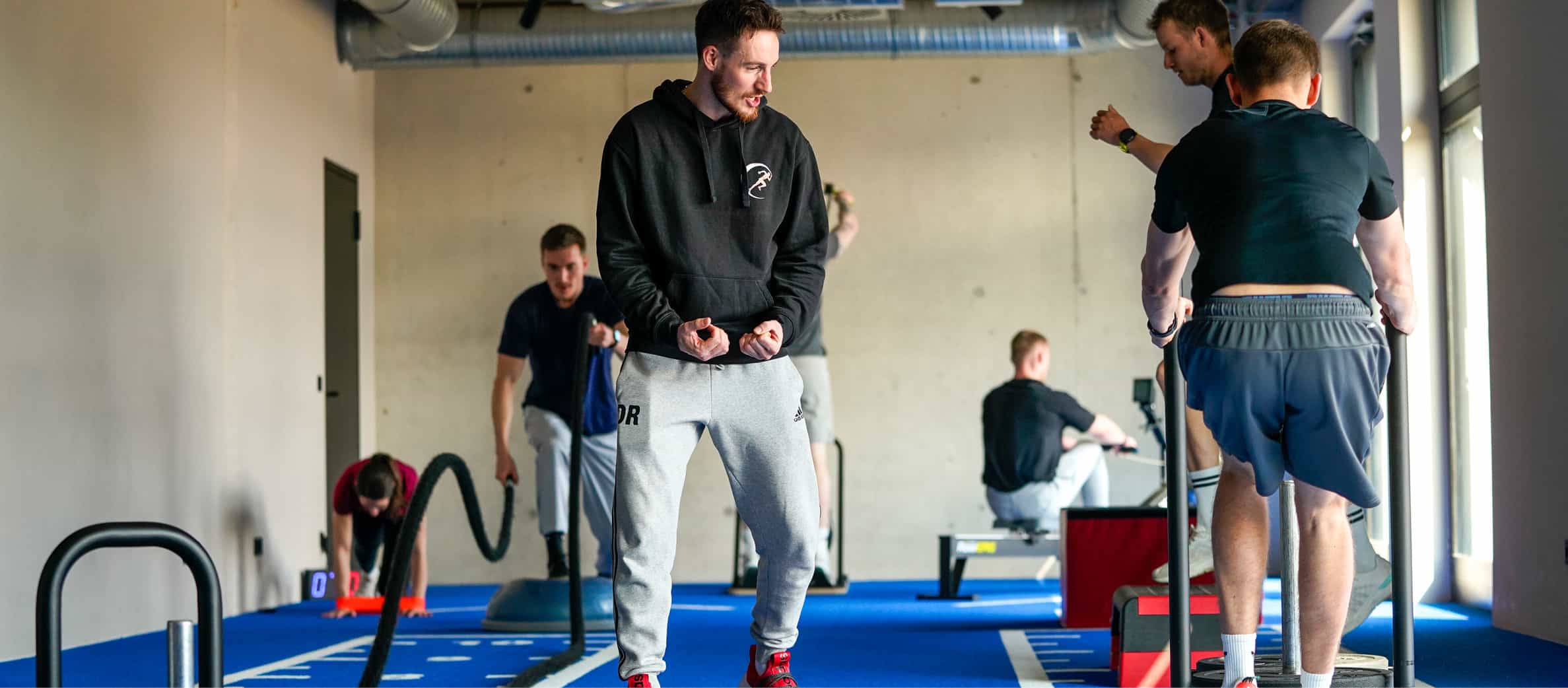 Coach Daniel Radis instruiert und motiviert eine Gruppe von Sportlern beim Zirkeltraining an verschiedenen Übungsstationen in der Community Class.