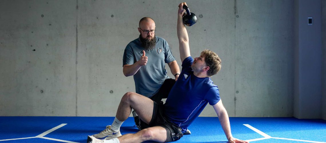 Coach Christoph Weber zeigt einem Sportler im Functional Training Kurs die korrekte Technik einer Übung mit der Kettlebell, um Verletzungen vorzubeugen und die Effizienz zu steigern.