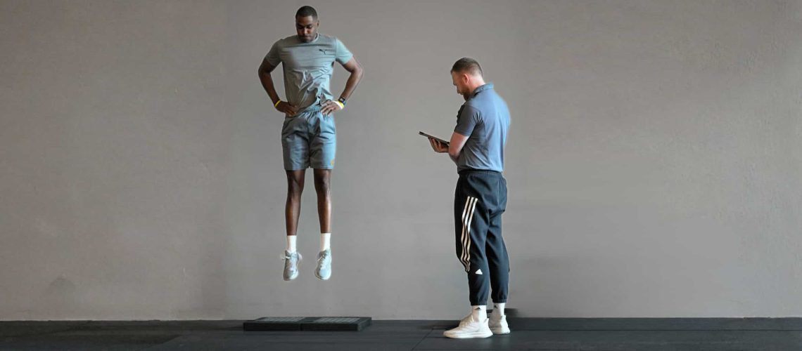 Plyometrisches Training in der späten Reha: Ein Athlet führt einen Sprung über einen Vault aus, während ein Coach Technik und Landung überwacht.